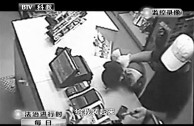 戴帽男子一手掐住加油站營業(yè)員，一手持發(fā)令槍指向另一營業(yè)員，要求“把錢給我裝起來”。