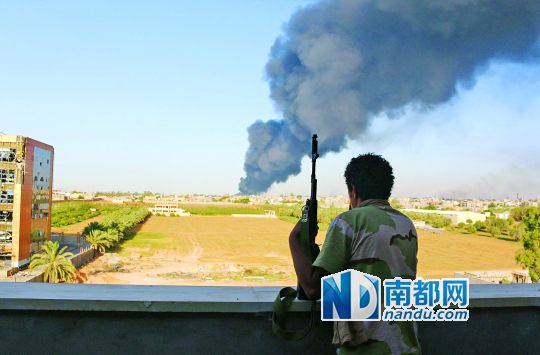 2日，利比亞首都的黎波里，一民兵武裝成員眺望被火箭彈擊中的儲油罐冒出濃煙。