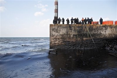 昨日，山東青島，清污人員正在海邊清理油污。