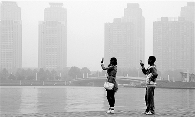 29日中午，鄭東新區(qū)如意湖畔，兩個(gè)年輕人拍攝霧霾中的景色。 鄭州晚報(bào)記者 馬健 圖