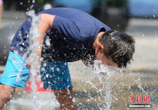 5月29日，一名小孩將頭伸向北京街頭的噴泉以降溫祛暑。