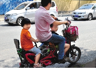 周先生騎著一輛低矮的電動車帶著一對兒女，很不安全。