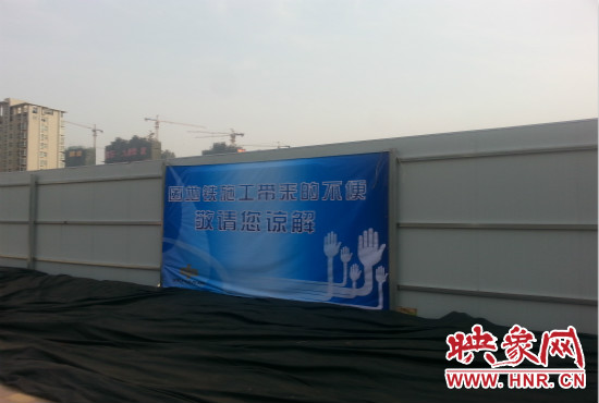 道路南側(cè)圍起了白色的圍擋，墻上標(biāo)示著“因地鐵施工帶來(lái)的不便敬請(qǐng)您諒解”的提示牌。