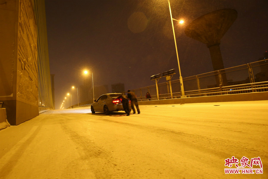 雪天路滑，汽車上橋打滑，兩名“推車人”幫助一輛私家車上坡。