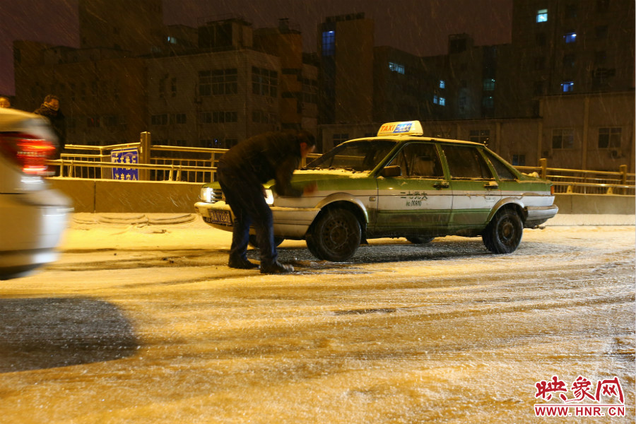 一位出租車司機在車輪前灑上雪，希望能增加輪胎的摩擦力。