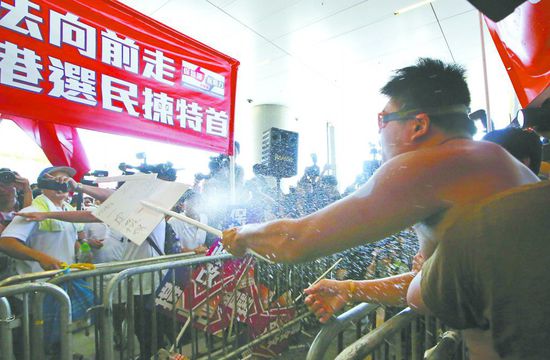 17日，在香港立法會(huì)外，一名反對(duì)政改的男子向支持派人群投擲標(biāo)牌。