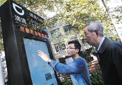10月15日，滴滴工作人員（左）指導乘客使用“滴滴車站”的電子屏預約出租車。