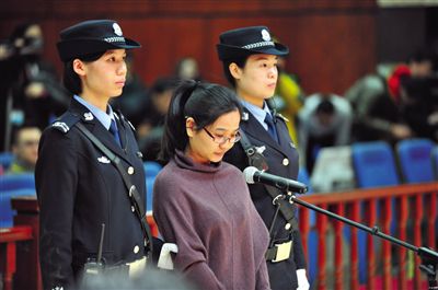 被告人盧梅低著頭，站在朝陽法院刑事審判庭的被告席上。